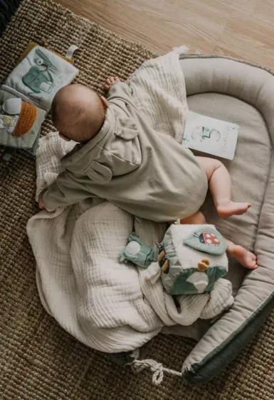 Bébé sur le ventre dans un coussin avec ses jouets