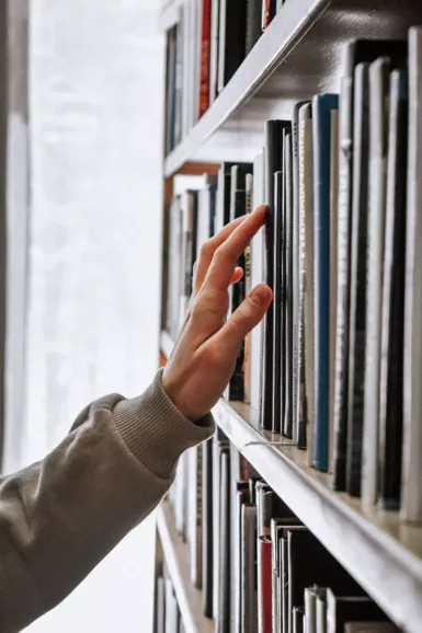 Personne tendant la main vers un rayon de bibliothèque