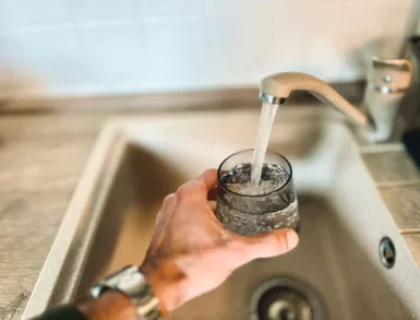 Une main remplissant un verre d'eau au robinet