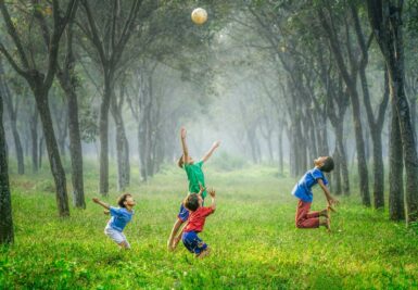 4 enfants jouant au ballon dans l'herbe